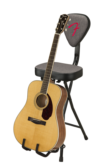 The image shows a black Fender guitar chair with a red logo on the backrest, designed for guitarists. It features a built-in guitar rest holding a natural wood-colored dreadnought acoustic guitar with a dark pickguard and spruce top. This folding chair combines seating and guitar storage, ideal for practice, performances, or studio use.