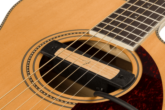 The image shows a close-up of an acoustic guitar focusing on the soundhole with decorative rosette, steel or nylon strings, light-colored soundboard, dark reddish-brown pickguard, part of the fretboard with markers, and the bridge area where strings anchor. The traditional design and wood grain highlight the craftsmanship and key features that enable the guitar to produce sound.