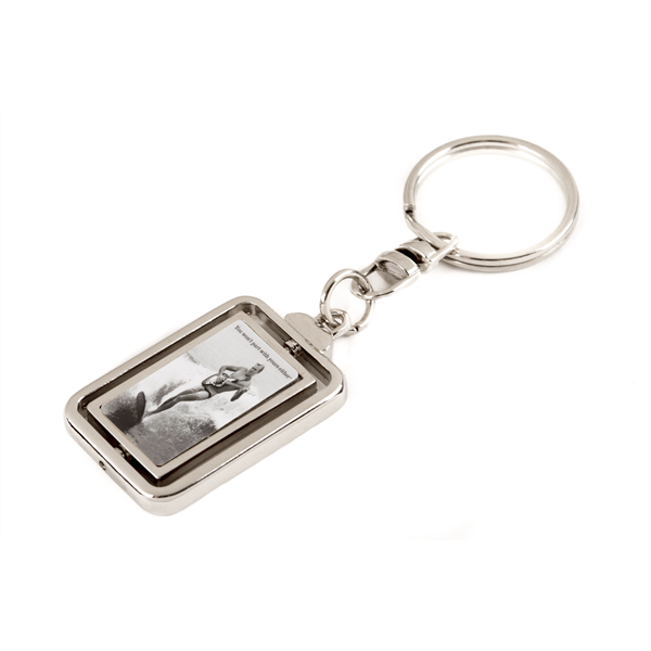 The image shows a music-themed keychain with a rectangular metal frame containing a black-and-white photo, likely of a musician or band. It is attached to a metal keyring by a chain link. This merchandise item is typical for music fans to show support and is commonly sold at music stores, concert venues, and online shops alongside other fan accessories.