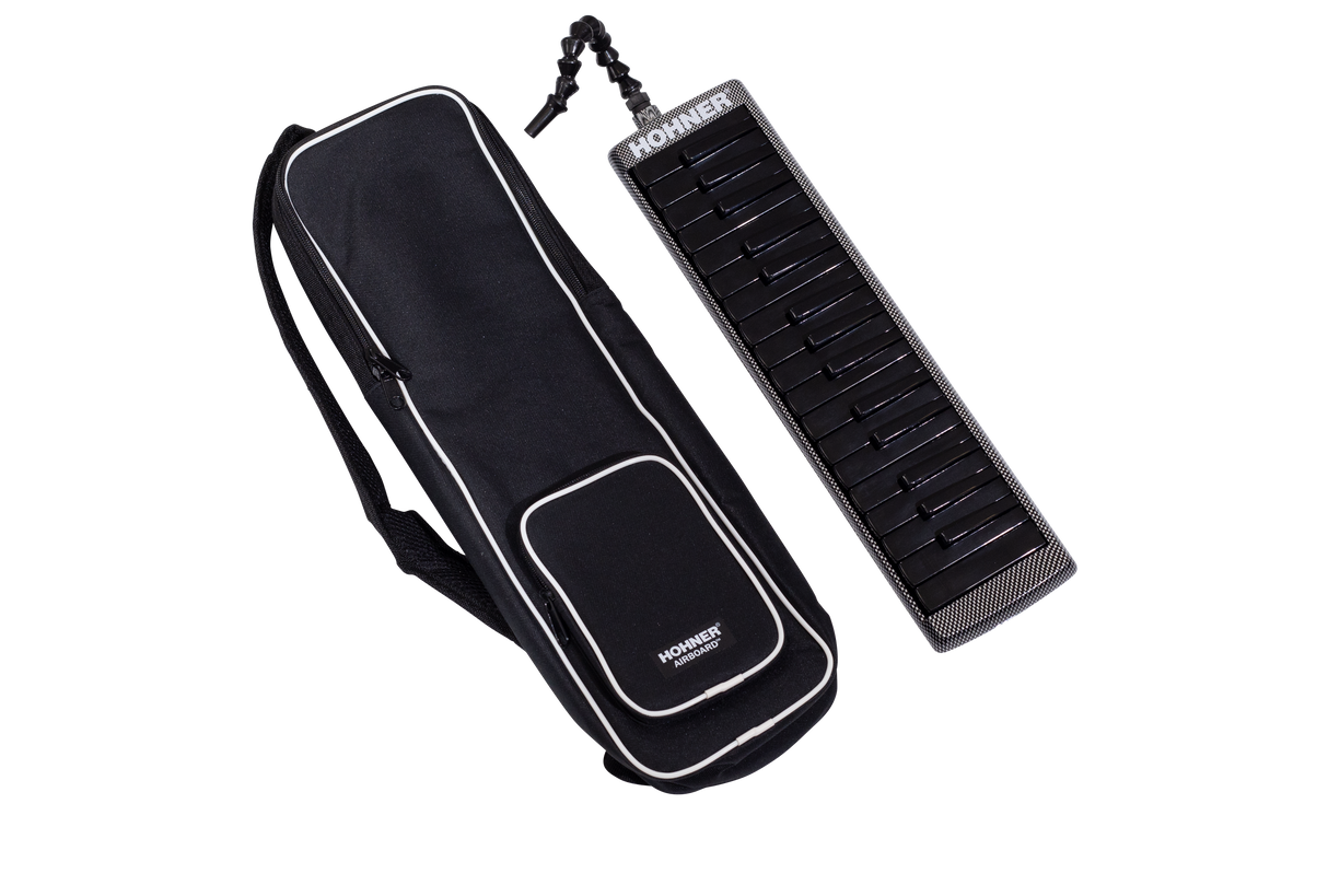 The image shows a black Hohner melodica with white and black piano-style keys alongside its black carrying case with white trim. The case has shoulder straps and a front pocket for easy transport. A flexible tube mouthpiece is attached to the melodica. This wind instrument produces sound by blowing air through the mouthpiece while pressing keys and is popular in music education and various genres for its portable, unique sound.