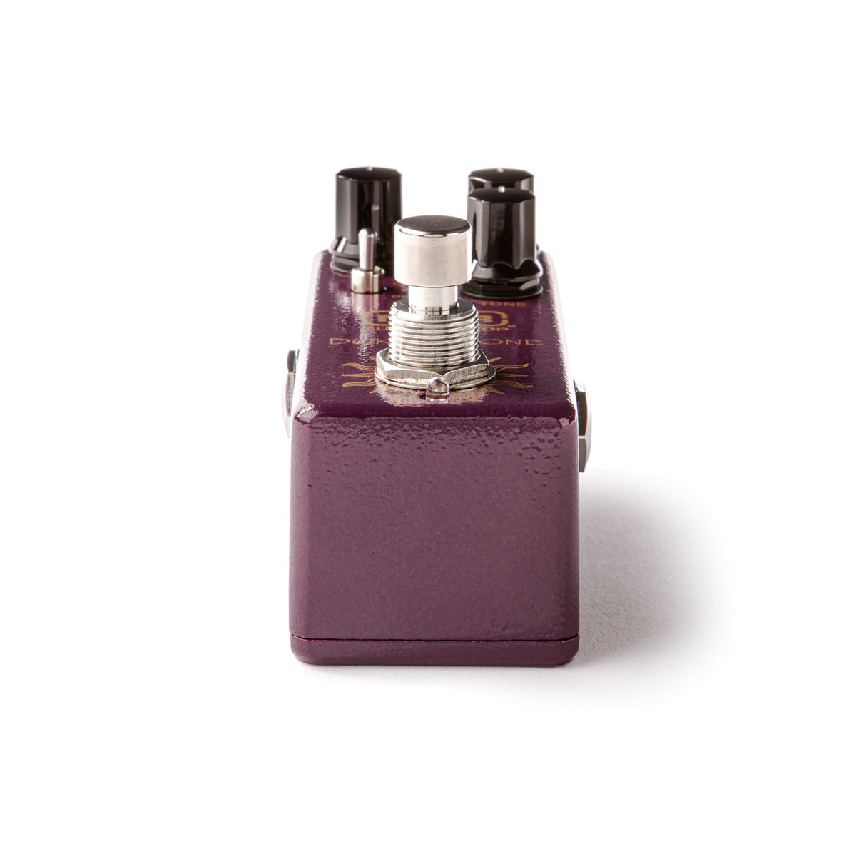 The image shows a guitar effects pedal with a purple/burgundy textured metal enclosure. It features four black input/output jacks on top, a central silver footswitch, and a compact, sturdy design typical of stompbox pedals. Used by guitarists to modify sound, its boutique appearance suggests a specialty product. This pedal is designed for floor use and enhances tone in live or recording settings.