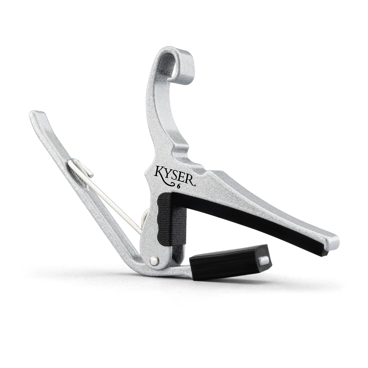 The image shows a KYSER guitar capo made of silver metal with black rubber padding. It features a spring-loaded clamp with a curved handle for easy one-handed use. The capo clamps across the guitar fretboard to raise the pitch of all strings simultaneously, allowing players to change keys with the same chord shapes. KYSER is a trusted brand known for reliable, quick-change capos.