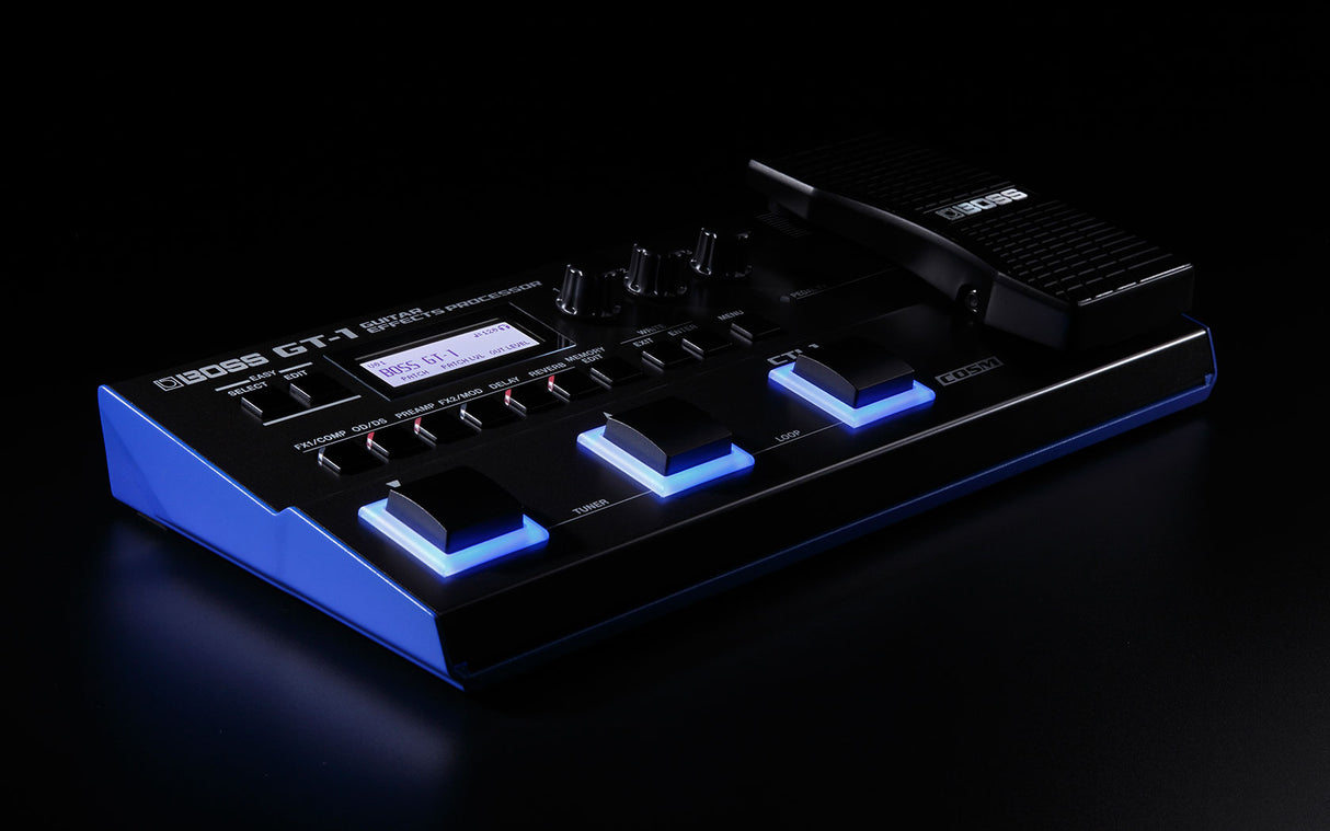 The image shows a BOSS GT-1 Guitar Effects Processor, a compact, floor-based multi-effects pedal with a black housing and blue LED accents. It features an LCD screen displaying patch info, multiple control knobs for effect settings, and three illuminated blue footswitches. Branded with BOSS and model GT-1, it offers versatile guitar effects and amp simulations in a sturdy design for both live and studio use.