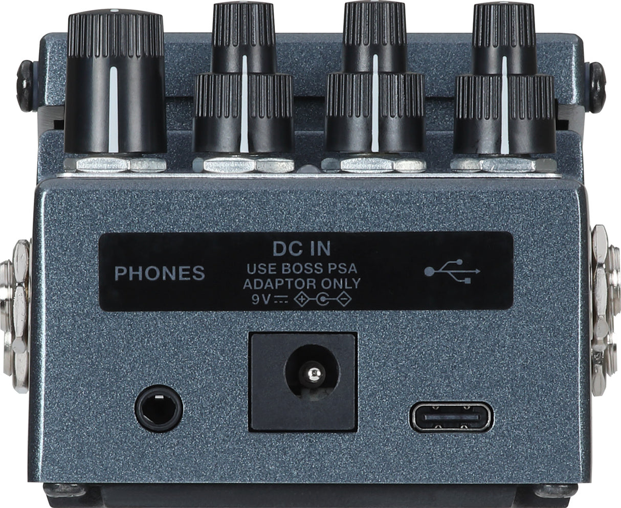 The image shows a BOSS guitar effects pedal with a blue/gray metal body, featuring eight control knobs in two rows, input/output jacks, a headphone output labeled "PHONES," a USB port, and a power input for a 9V BOSS PSA adapter. Designed as a stomp-box, it allows musicians to activate effects by foot and is used to modify and enhance the sound of electric guitars, basses, and other instruments.
