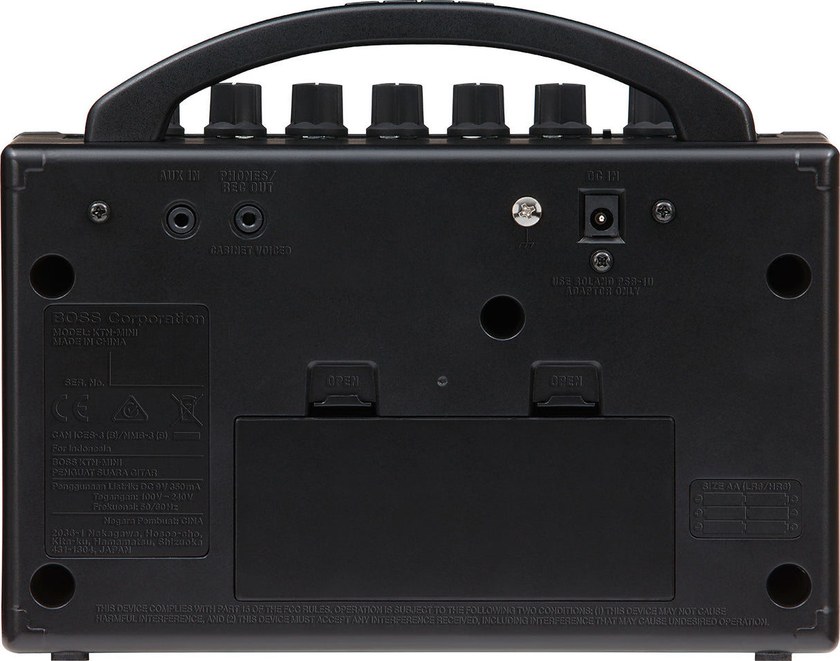 The image shows the back panel of a BOSS Katana Mini (KTN-MINI) guitar amplifier, featuring AUX IN and PHONES/REC OUT jacks, a DC power input, a USB port, ventilation holes, regulatory labels, and rubber feet. This compact amplifier supports silent practice with headphones, playing along via auxiliary input, and USB connectivity for recording or updates.