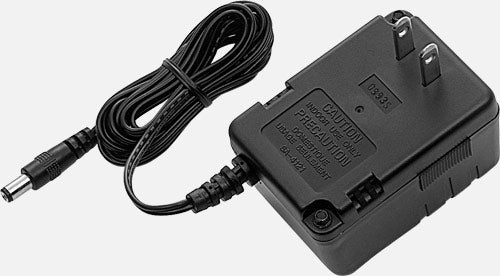 The image shows a black power adapter with ventilation grilles, standard AC plug prongs, a long power cord, and a DC barrel connector. Text with specifications is printed on the housing. This adapter is likely used to power electronic musical instruments or effects pedals that require external DC power, common in music equipment like keyboards, synthesizers, and guitar pedals.