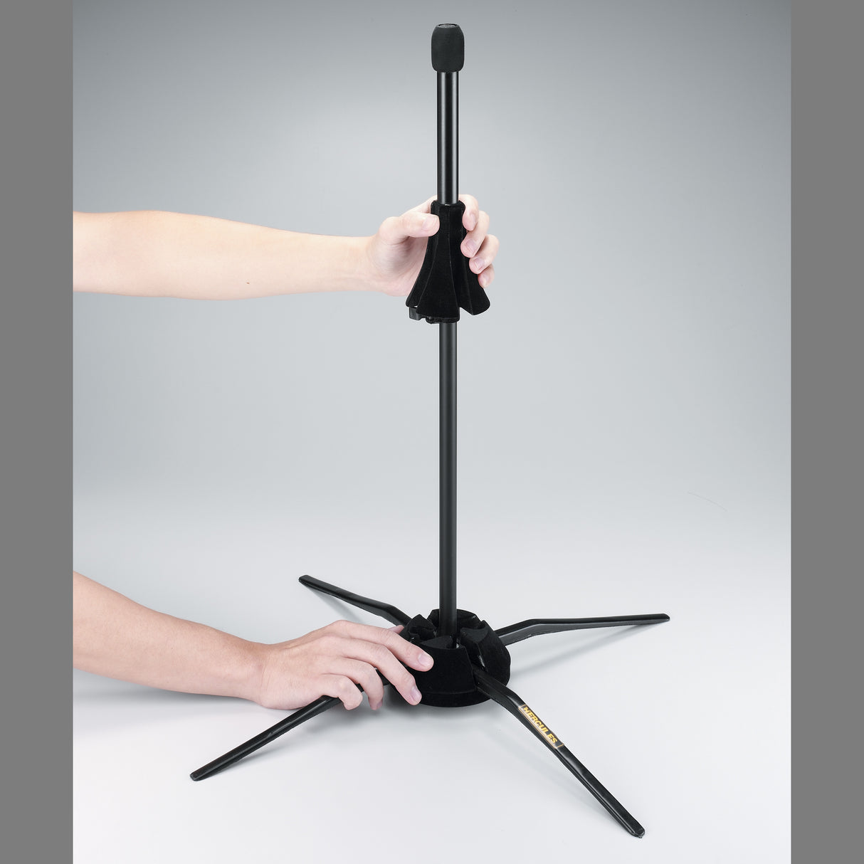 A black trombone stand being adjusted by a human on a grey background
