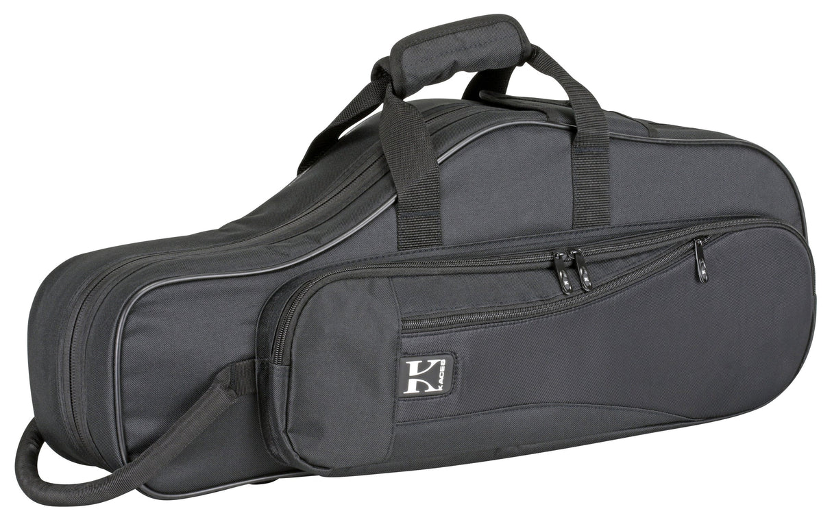 The image shows a charcoal gray soft-sided gig bag for a tenor saxophone or similar wind instrument. It has multiple zippered pockets, padded handles, an adjustable shoulder strap, and a white logo featuring a "K" or similar letter. The durable, reinforced case has an elongated curved shape matching the instrument, designed for lightweight, portable protection and accessory storage.