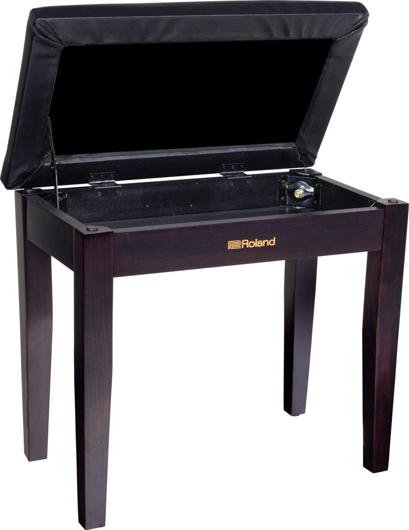 The image shows a Roland piano bench with a dark wood finish and gold Roland logo. It features a padded black seat that lifts to reveal a fabric-lined storage compartment. The bench has sturdy wooden legs and an elegant, professional design, suitable for home or studio use. It offers adjustable height for comfortable playing and convenient storage for sheet music and accessories.