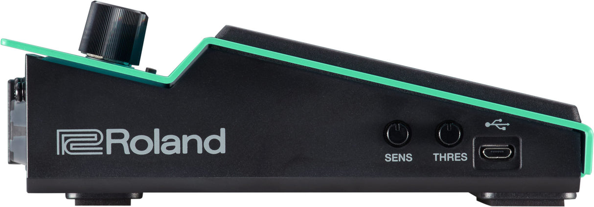 The image shows a black Roland electronic drum module with green accents, featuring two control knobs labeled "SENS" and "THRES," a USB port, and a trigger input jack. This module converts drum pad or trigger signals into electronic sounds, allowing sensitivity and threshold adjustments to optimize response. It connects to computers via USB for recording and integration with digital audio workstations.