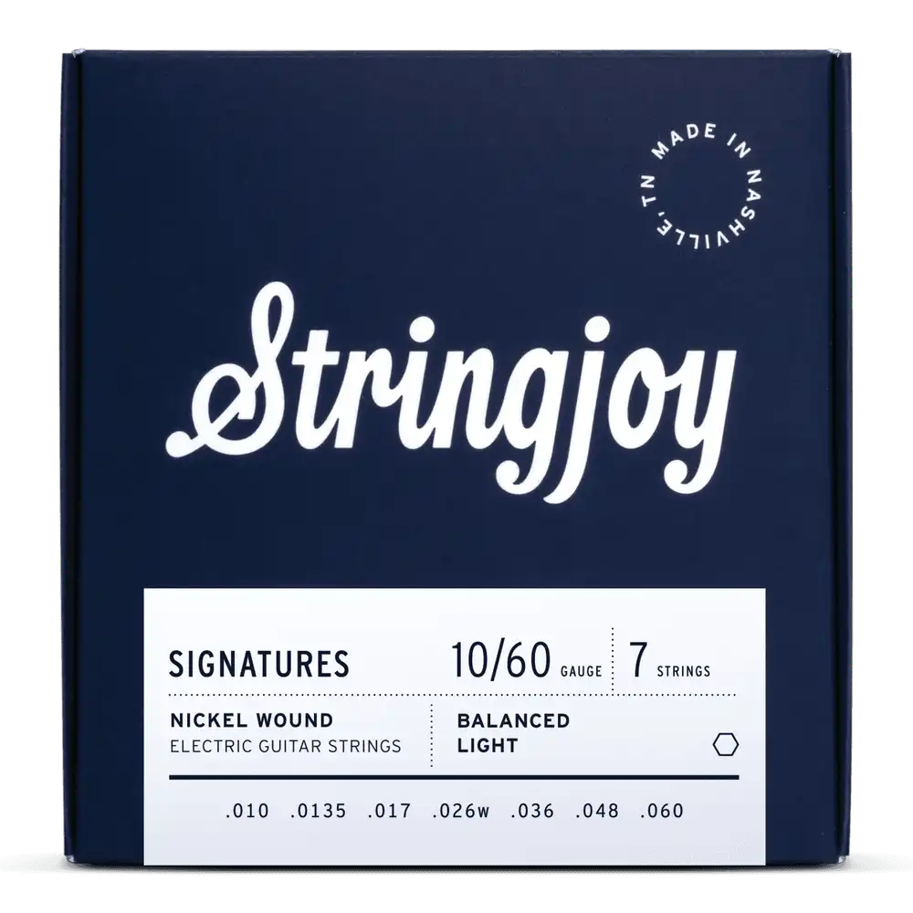 The image shows a package of Stringjoy "Signatures" 7-string electric guitar strings, gauge 10-60, nickel wound with balanced light tension. The deep navy box features white lettering, an elegant script logo, and "Made in Nashville, N.L." marking. This premium set is designed for extended range guitars, offering comfortable playability and tone across all seven strings.