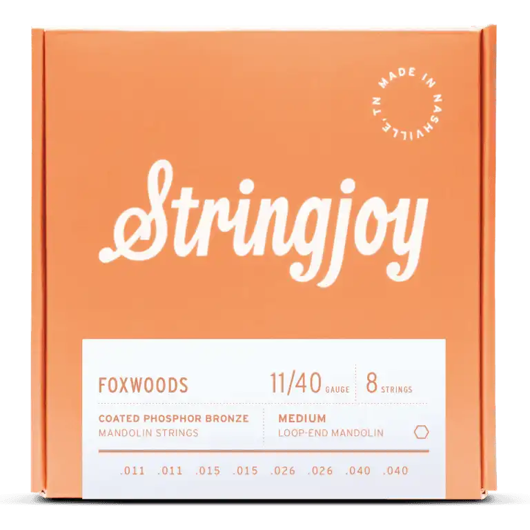 The image shows a package of Stringjoy Foxwoods Coated Phosphor Bronze mandolin strings in medium gauge 11/40. It contains 8 medium loop-end strings (.011, .011, .015, .015, .026, .026, .040, .040) in a coral-orange box with white script branding. A "Made in Nashville" logo appears in the top right, and product details are on a white label at the bottom. The coated strings offer enhanced tone and durability.