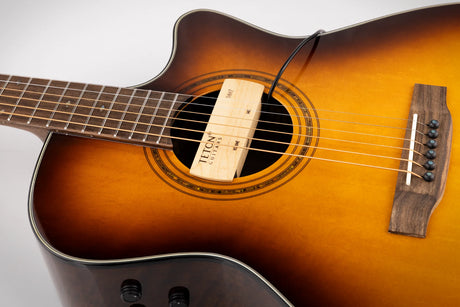 The image shows a Teton dreadnought acoustic-electric guitar with a sunburst finish fading from dark brown/black edges to a golden center. It features a round sound hole with a decorative rosette, a dark wood bridge with white pins, a dark fretboard with inlays, and steel strings. Control knobs on the lower bout indicate electronics for amplification. The "TETON GUITARS" label is visible inside the sound hole.