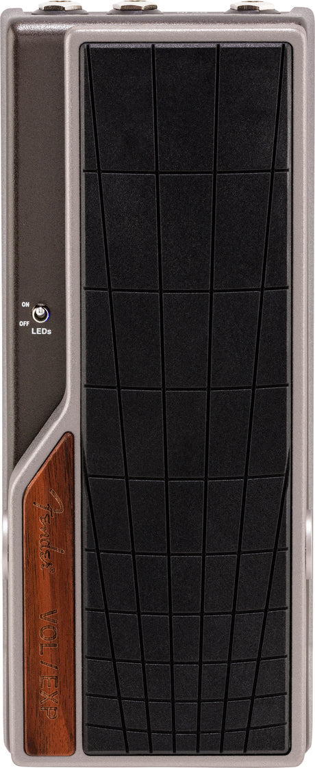 The image shows a Fender volume/expression pedal with a sleek gray metal housing and a large black textured footplate. It features the Fender logo on a wooden panel and an ON/OFF LED switch. The rocker-style design lets guitarists control volume or effects parameters like wah and delay for dynamic, expressive playing. Fender is a trusted brand known for quality guitar gear.