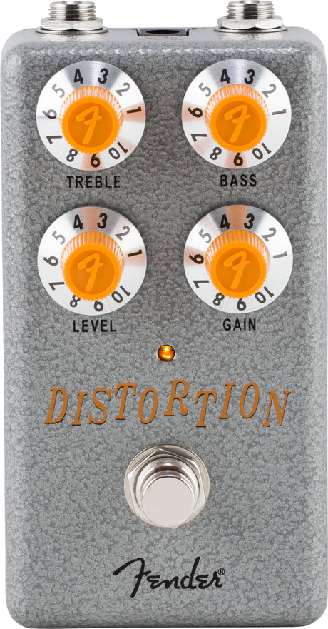 The image shows a Fender distortion pedal with a gray textured metal casing and four orange knobs labeled Treble, Bass, Level, and Gain, each numbered 0-10 and featuring the Fender "F" logo. It includes input/output jacks, a footswitch, an LED indicator, and the Fender script logo. This pedal modifies electric guitar sound by adding distortion and overdrive effects.