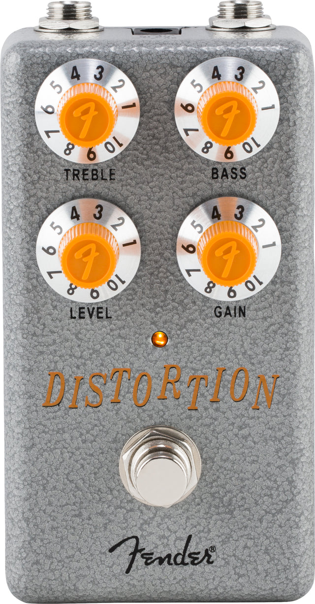 The image shows a Fender distortion pedal with a gray textured metal casing and four orange knobs labeled Treble, Bass, Level, and Gain, each numbered 0-10 and featuring the Fender "F" logo. It includes input/output jacks, a footswitch, an LED indicator, and the Fender script logo. This pedal modifies electric guitar sound by adding distortion and overdrive effects.