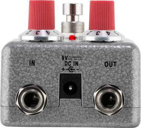 The image shows a guitar effects pedal, likely a distortion or overdrive type, with two red-topped control knobs, a central footswitch, input/output jacks labeled "IN" and "OUT," a 9V DC power input, a small red LED indicator, and a textured gray/silver metal casing. This pedal modifies electric guitar sound by adding distortion or overdrive between the guitar and amplifier.