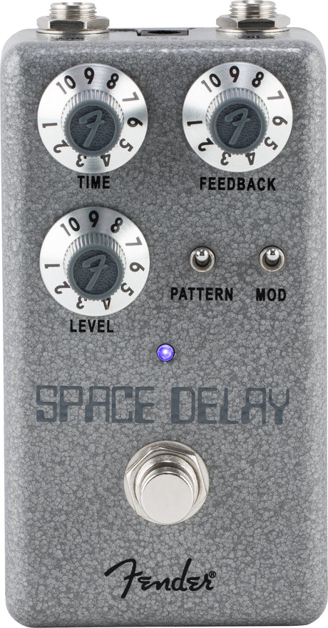 The image shows a Fender Space Delay guitar effects pedal with a compact gray/silver textured design. It has three main knobs (TIME, FEEDBACK, LEVEL), two smaller toggle switches (PATTERN, MOD), input/output jacks, a footswitch, a blue LED indicator, and the Fender logo. This digital delay pedal creates versatile echo and modulation effects, ideal for pedalboards.