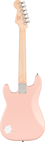 The image shows the back of a pink/coral Squier electric guitar with a maple neck and six chrome tuning pegs on the headstock. It features a contoured Stratocaster-style body, a chrome neck plate for the bolt-on neck, and a battery or control cavity cover on the lower bout. The finish is solid, highlighting the classic design typical of Squier, Fender’s affordable brand.