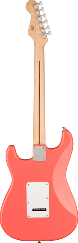 The image shows the back of a coral pink Stratocaster-style electric guitar with a glossy body and classic contours. It features a natural wood neck and headstock with six chrome tuning pegs in a 6-in-line layout. Visible are a white tremolo cavity cover, a chrome neck plate, and a truss rod adjustment slot. The bolt-on neck design and hardware suggest a Fender or similar model.