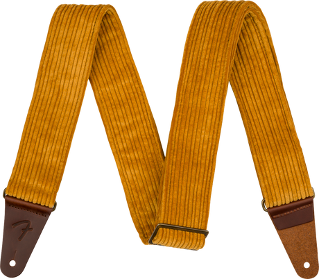 The image shows a guitar strap made of golden yellow corduroy with a ridged texture and brown leather ends, one embossed with a Fender logo. It features an adjustable metal slide buckle and a vintage-inspired design. This strap combines style and function, supporting the guitar when playing standing up while adding a retro, fashionable look.