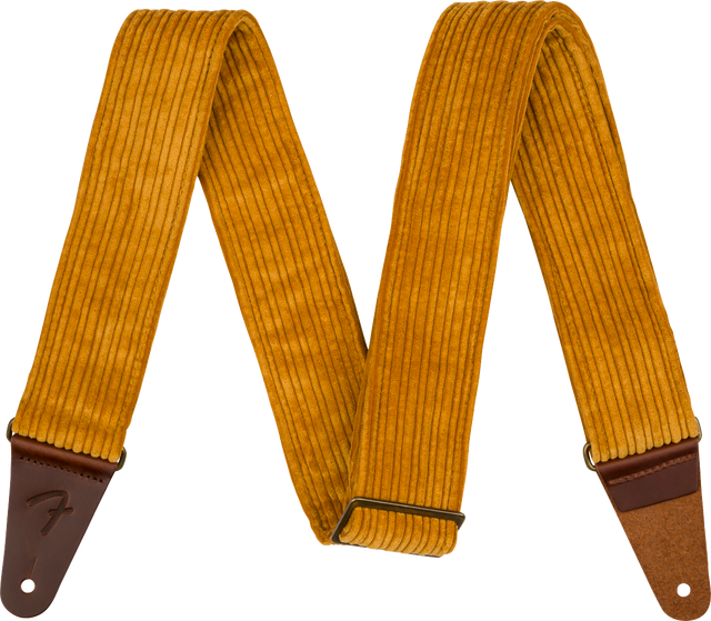 The image shows a guitar strap made of golden yellow corduroy with a ridged texture and brown leather ends, one embossed with a Fender logo. It features an adjustable metal slide buckle and a vintage-inspired design. This strap combines style and function, supporting the guitar when playing standing up while adding a retro, fashionable look.