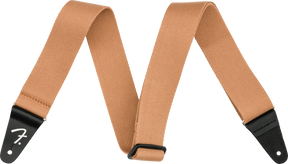 The image shows a tan/brown woven cotton or canvas guitar strap with black leather Fender-branded end tabs. It has an adjustable length and a classic, functional design. This essential accessory helps guitarists and bassists comfortably play while standing by distributing the instrument’s weight across the shoulder and torso, suitable for various musical styles and performance settings.
