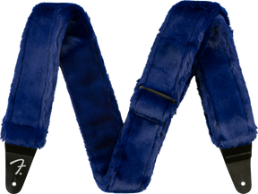 The image shows a guitar strap covered in luxurious blue faux fur with black leather ends, one displaying the Fender logo. This plush, furry strap combines comfort and style, offering extra padding for long playing sessions while making a bold, eye-catching statement with its deep blue color and soft texture.