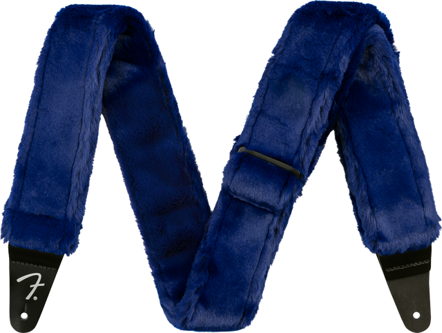 The image shows a guitar strap covered in luxurious blue fur or faux fur with black leather ends, one displaying the Fender logo. This plush, furry strap combines comfort and style, offering extra padding for long playing sessions while making a bold, eye-catching statement with its deep blue color and soft texture.