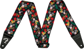 The image shows a Fender guitar strap with a black background featuring a festive pattern of red-nosed reindeer, red poinsettias, green holly leaves, white snowflakes, and gold Fender logos. It has black leather ends, one displaying the white Fender "F" logo, with holes for attaching to guitar strap pins. This seasonal accessory blends holiday designs with classic Fender branding.