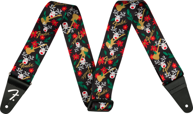 The image shows a Fender guitar strap with a black background featuring a festive pattern of red-nosed reindeer, red poinsettias, green holly leaves, white snowflakes, and gold Fender logos. It has black leather ends, one displaying the white Fender "F" logo, with holes for attaching to guitar strap pins. This seasonal accessory blends holiday designs with classic Fender branding.