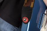 The image shows a red circular strap lock button attached to a blue electric guitar body. A brown leather guitar strap with yellow/gold trim is secured to the guitar using this locking mechanism. Strap locks prevent accidental strap detachment, protecting the guitar from falls. This accessory is popular among guitarists, especially when playing standing up, ensuring the instrument stays securely attached to the strap.