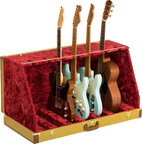 The image shows a professional guitar display case with a textured golden-yellow exterior and plush red velvet interior. It holds multiple guitars, including Fender-style electric guitars in black, cream, and blue, plus a natural wood acoustic guitar. The case features metal reinforcements, secure latches, and compartments for safe storage and display, ideal for musicians, collectors, or music stores.