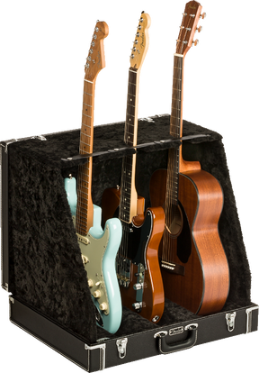 The image shows a professional black hard case/display stand with plush lining designed to hold and display multiple guitars. It securely supports three guitars: a light blue Stratocaster-style electric, a black electric, and a natural wood dreadnought acoustic. The sturdy case features metal latches and neck supports, ideal for musicians, collectors, stores, or studios needing safe, accessible multi-guitar storage.