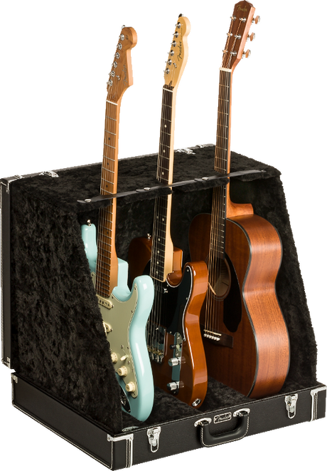 The image shows a professional black hard case/display stand with plush lining designed to hold and display multiple guitars. It securely supports three guitars: a light blue Stratocaster-style electric, a black electric, and a natural wood dreadnought acoustic. The sturdy case features metal latches and neck supports, ideal for musicians, collectors, stores, or studios needing safe, accessible multi-guitar storage.