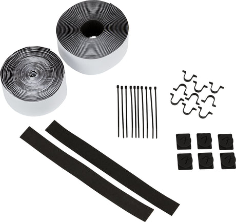 The image shows a piano or keyboard maintenance kit containing two rolls of adhesive tape or felt strips, black felt cushioning strips, six small black repair clips, thin black rods or pins, and small curved wire pieces like springs or clips. These specialized parts are used for regulation, repair, and maintenance of piano or keyboard actions, essential for technicians servicing acoustic and digital instruments.
