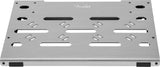The image shows a Fender pedalboard, a flat, silver, brushed-metal platform with the Fender script logo. It features various slots and mounting holes for securing different guitar effects pedals, ventilation openings for heat dissipation, and rubber feet to prevent slipping. This sturdy, professional board helps guitarists organize and transport multiple pedals in a customizable, tidy setup.