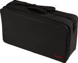 The image shows a black Fender gig bag, a rectangular, padded soft case made of durable fabric with zippered compartments and reinforced handles. It features the red Fender logo on the bottom right. Designed for carrying musical gear like amplifier accessories or pedals, it has a professional, utilitarian style typical of Fender’s musician equipment cases.