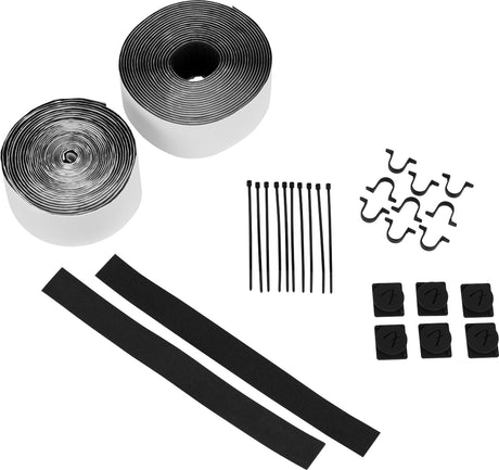 The image shows a cable management kit for musical setups, including two rolls of black and white hook-and-loop tape, black cable ties, cable clips with routing channels, and curved wire guides. This kit helps musicians organize instrument, power, and patch cables to prevent tangling, reduce noise, enhance safety, and streamline setup and teardown for live or studio use.