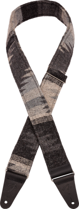 The image shows a guitar strap with a grayscale woven pattern in shades of gray and black. It has dark leather or synthetic leather end tabs with adjustment holes for attaching to a guitar. This strap combines functionality and style, allowing musicians to play standing while supporting the instrument’s weight. Its modern design and adjustable length offer comfort and a sophisticated look that suits various guitars and playing styles.