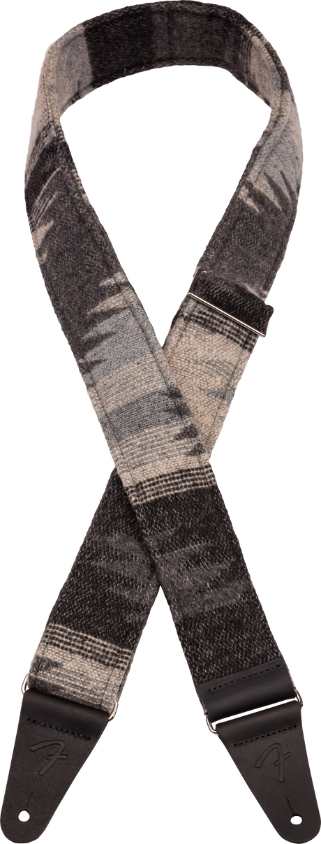 The image shows a guitar strap with a grayscale woven pattern in shades of gray and black. It has dark leather or synthetic leather end tabs with adjustment holes for attaching to a guitar. This strap combines functionality and style, allowing musicians to play standing while supporting the instrument’s weight. Its modern design and adjustable length offer comfort and a sophisticated look that suits various guitars and playing styles.