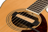 The image shows a close-up of an acoustic guitar focusing on the soundhole with decorative rosette, steel or nylon strings, light-colored soundboard, dark reddish-brown pickguard, part of the fretboard with markers, and the bridge area where strings anchor. The traditional design and wood grain highlight the craftsmanship and key features that enable the guitar to produce sound.