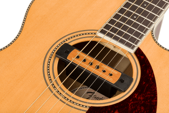 The image shows a close-up of an acoustic-electric guitar focusing on the soundhole and part of the fretboard. It features a natural wood finish, a circular rosette with dotted inlay, a wooden-colored humbucker pickup in the soundhole, a dark wood fretboard with visible frets, a reddish-brown tortoiseshell pickguard, and steel strings running over the pickup and neck.