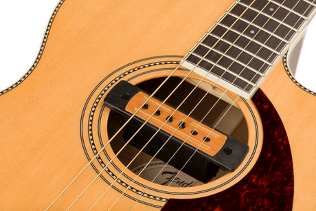 The image shows a close-up of an acoustic-electric guitar focusing on the soundhole and part of the fretboard. It features a natural wood finish, a circular rosette with dotted inlay, a wooden-colored humbucker pickup in the soundhole, a dark wood fretboard with visible frets, a reddish-brown tortoiseshell pickguard, and steel strings running over the pickup and neck.