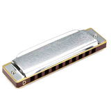 The image shows a "Folk Master" diatonic harmonica in the key of D. It features a chrome-plated metal cover with etched designs, a rich brown wooden comb, and multiple holes for playing notes. The cover plates are secured with screws, revealing metal reed plates inside. This classic harmonica design is commonly used in folk, blues, country, and rock music, suitable for beginners and intermediate players.