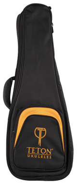 The image shows a TETON UKULELES padded soft gig bag for a ukulele. It is black with orange/amber trim and features a full-length zipper, a front pocket with the Teton logo, carrying handles, and durable fabric. The case has a teardrop shape to fit a ukulele’s body, offering lightweight protection and easy transport, with branding indicating Teton as the manufacturer.
