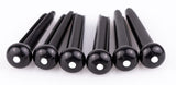 The image shows six black guitar bridge pins, likely made of plastic or ebony, each with a small white dot on the rounded end. These pins secure the strings at the bridge of an acoustic guitar by holding the string ball ends in place. Their tapered design ensures a snug fit, while the rounded tops make removal easy. They are common replacement parts for maintaining acoustic guitars.