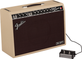 The image shows a Fender Deluxe Reverb-Amp guitar amplifier with a blonde/cream tolex exterior and dark brown grille. The control panel features multiple knobs for volume, treble, bass, reverb, and vibrato, with two input jacks labeled "NORMAL." A black footswitch is connected, and a black leather handle is on top. The "Tone Master" badge is visible on the lower right. This classic tube combo amp is known for its warm tone and built-in spring reverb.