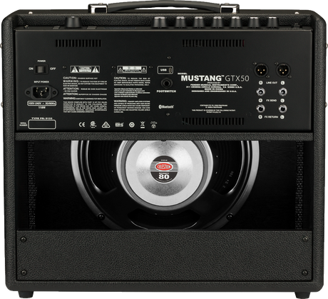 The image shows the back panel of a Fender Mustang GTX50 guitar amplifier. It features a Celestion speaker visible through the open back, multiple I/O options including XLR outputs, FX loop, USB, footswitch, and Bluetooth connectivity. The amp is covered in black tolex with a sturdy handle and supports 100V-240V AC power. This 50-watt digital modeling amp offers versatile tones and modern features for practice and performance.