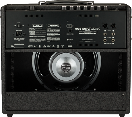 The image shows the rear view of a Fender Mustang GTX100 guitar amplifier. It features an open-back design with a visible 12-inch Celestion speaker, labeled "MUSTANG GTX100." Connectivity includes XLR outputs, line out, FX send/return, footswitch jack, USB, Bluetooth, AC power input, and an on/off switch. The amp has black tolex, metal corner protectors, and a handle. It is a 100-watt digital modeling amp from Fender’s Mustang series.